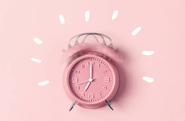 Classic pink alarm clock ringing at seven oclock against pastel pink background — Stock Photo, Image