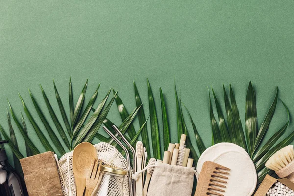 Sıfır atık. Pamuk torbası, bambu kabı, cam kavanoz, bambu diş fırçası, saç fırçası ve yeşil arka planda pipet. — Stok fotoğraf
