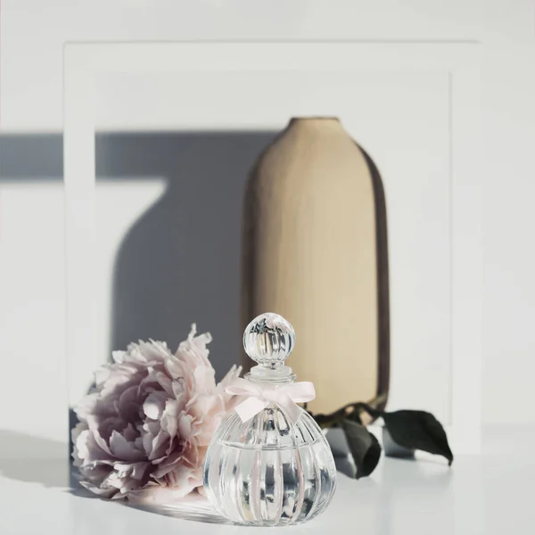 Fleur rose poivrée, flacon de parfum, vase et cadre en bois blanc contre mur blanc — Photo