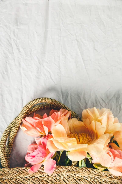 Flat-lay de hermosas flores de peonía en bolsa de paja sobre fondo de mantel de lino gris — Foto de Stock