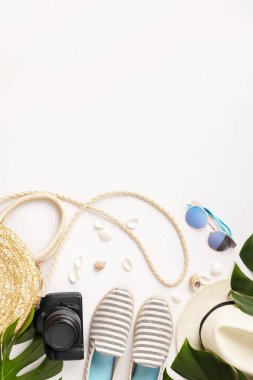 Hasır şapka, kamera, çanta, yaz ayakkabıları, güneş gözlükleri, kabuklar ve tropikal yapraklar beyaz arka planda, üst manzara.