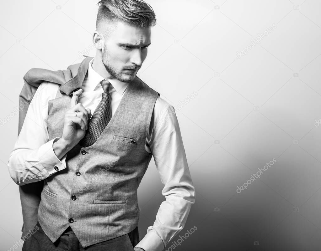 Handsome young elegant man in grey classic vest pose against studio background. Black-white photo.