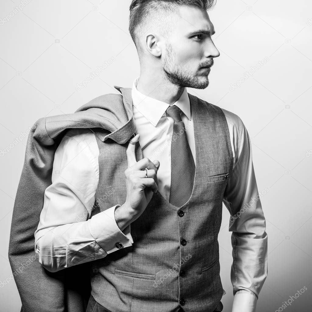 Handsome young elegant man in grey classic vest pose against studio background. Black-white photo.