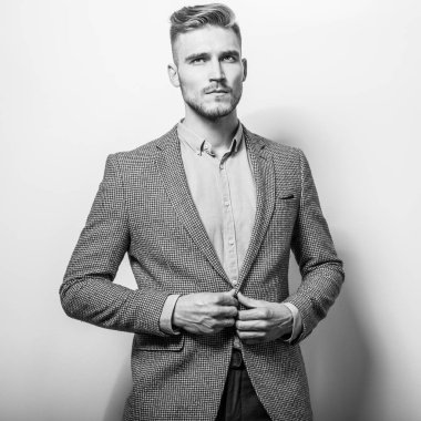 Zarif yakışıklı genç gri ceketli poz studio arka planı. Siyah-beyaz fotoğraf.