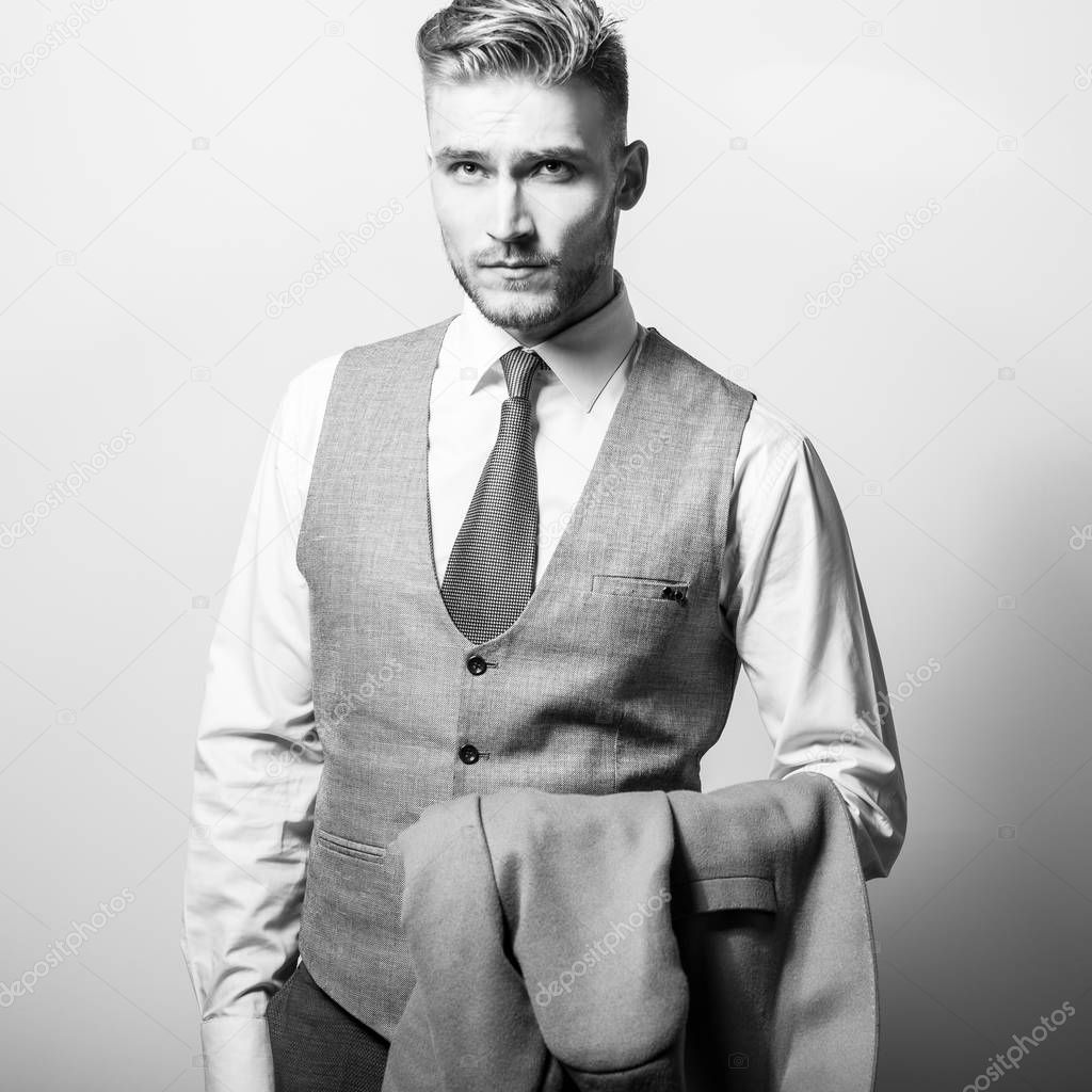 Handsome young elegant man in grey classic vest pose against studio background. Black-white photo.