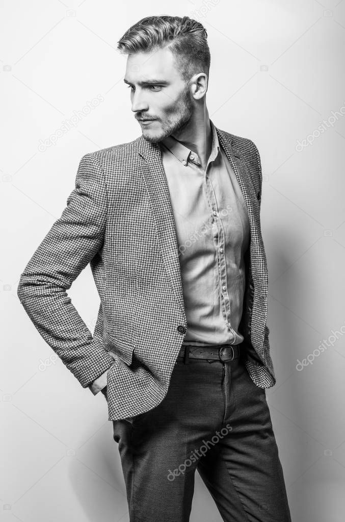 Handsome young elegant man in grey jacket pose against studio background. Black-white photo.