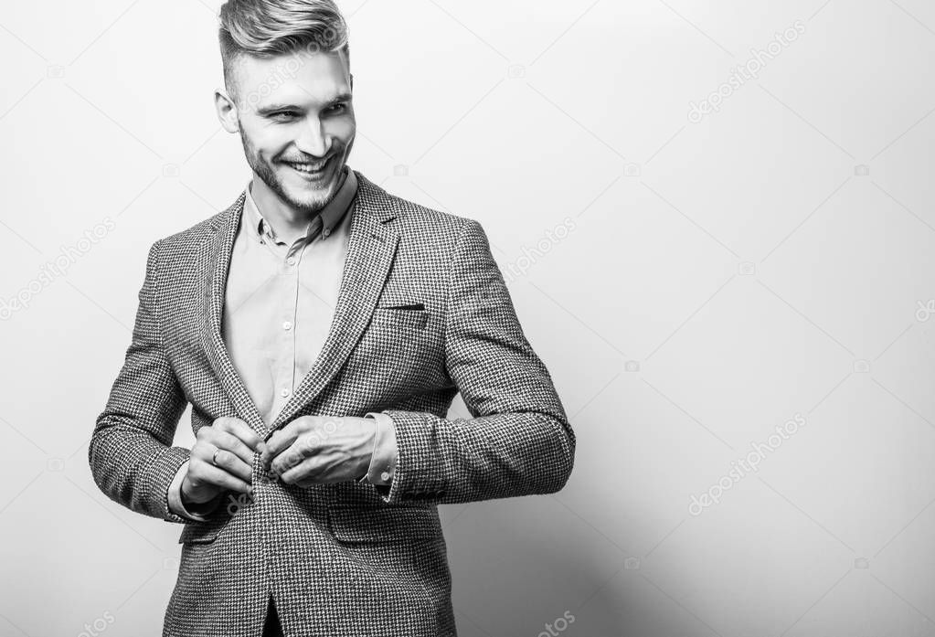Handsome young elegant man in grey jacket pose against studio background. Black-white photo.