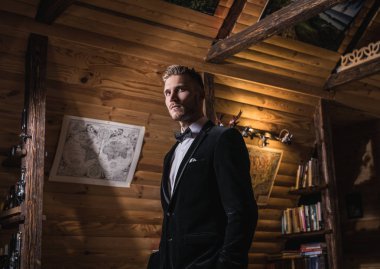 Zarif yakışıklı genç kostüm ve papyon poz karşı ev iç.