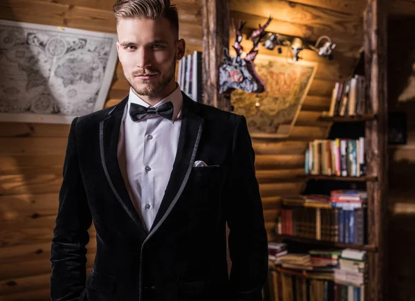 Zarif yakışıklı genç kostüm ve papyon poz karşı ev iç.