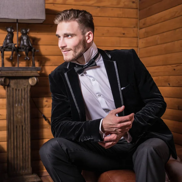 Zarif yakışıklı genç kostüm ve papyon poz karşı ev iç.