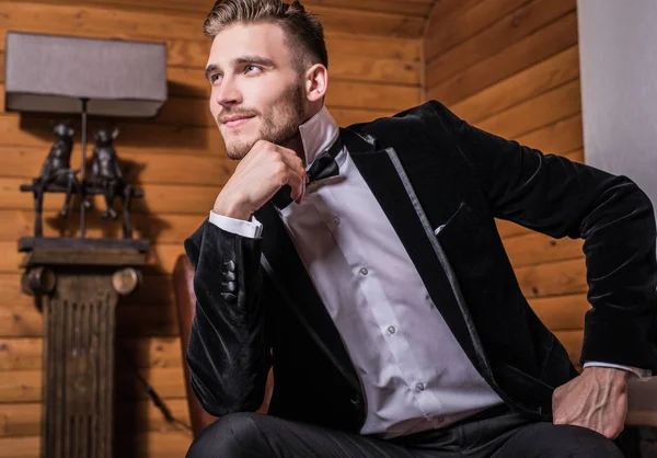 Zarif yakışıklı genç kostüm ve papyon poz karşı ev iç.