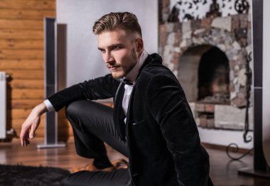 Zarif yakışıklı genç kostüm ve papyon poz karşı ev iç.