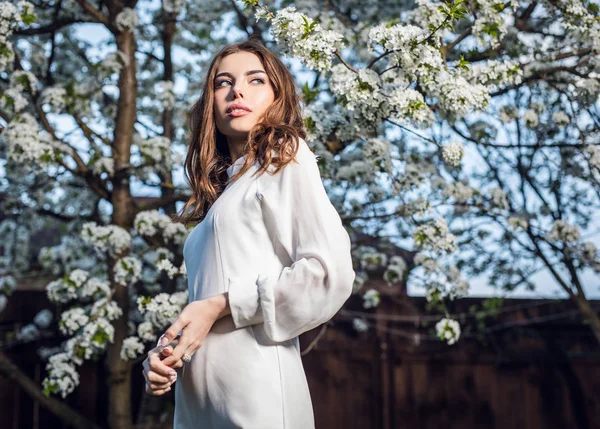 咲く桜に対して秋の庭でポーズをとって白いドレスの美しい若い女性の肖像画 — ストック写真