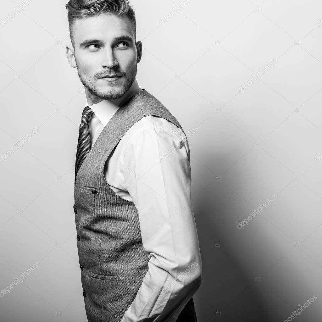 Handsome young elegant man in grey classic vest pose against studio background.