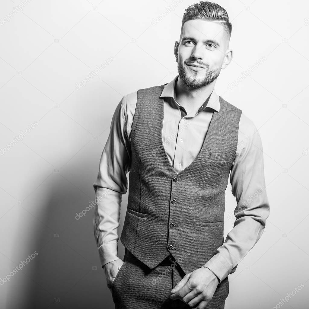 Handsome young elegant man in grey classic vest pose against studio background.