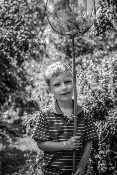 夏の庭でポーズの蝶のためのネットで幸せな男の子の屋外のポートレート 白黒写真 — ストック写真