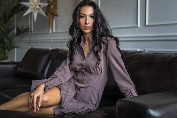 Beautiful young brunette woman in stylish dress pose in modern interior.