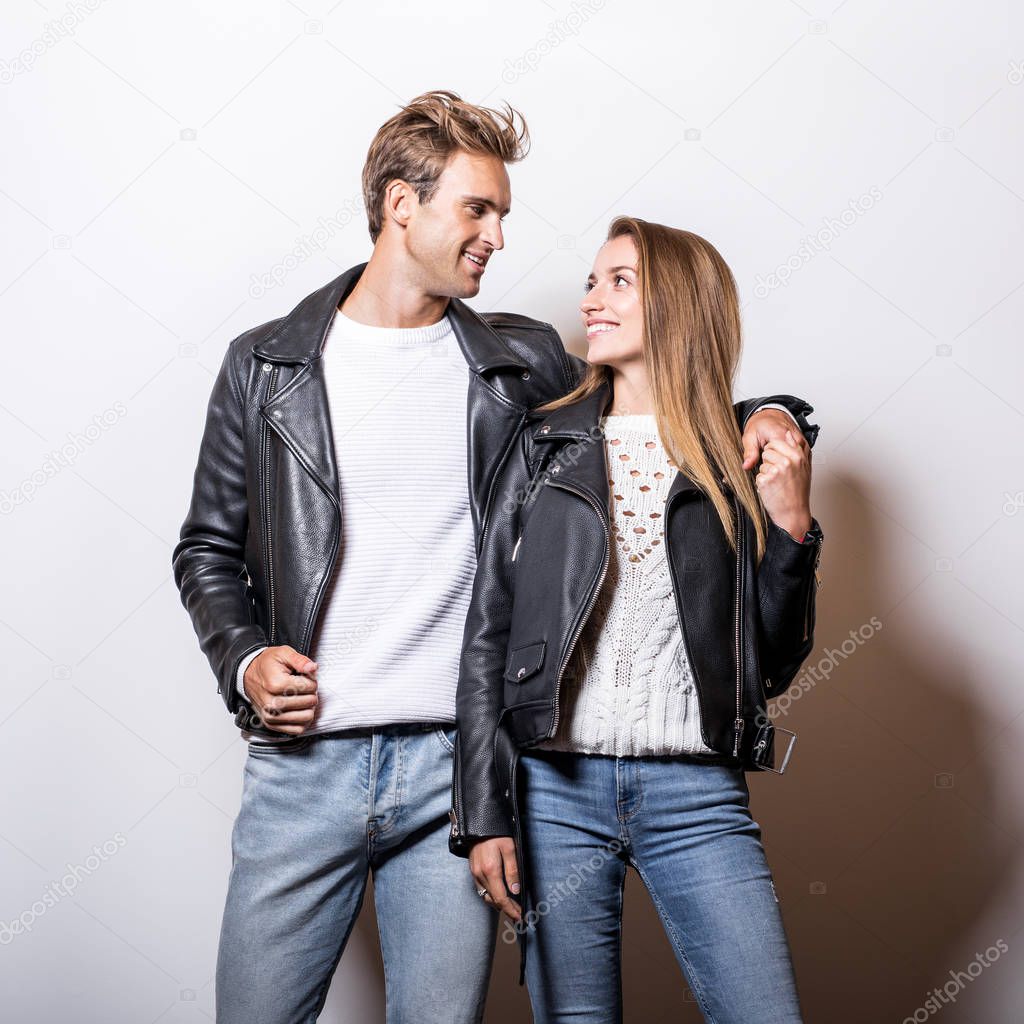 Young beautiful couple in black leather jackets pose in studio.