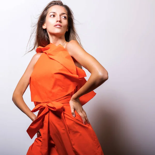 スタジオでオレンジ色のドレスポーズの若いモデルの女性 — ストック写真