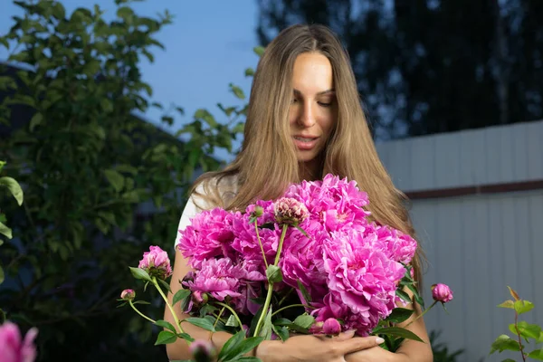 Молодая девушка в вечернем саду наслаждается букетом розовых пионов . — стоковое фото