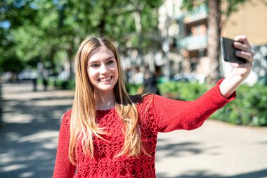 Güzel sarışın kadın selfies bir şehir parkında yapma.