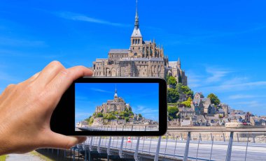 Akıllı telefonlu bir kadın Mont Saint Michel, Fransa 'nın fotoğrafını çekiyor. Turizm konsepti.