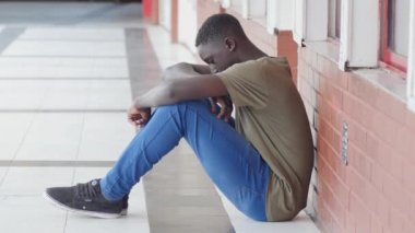 Zorbalık okul. Okul koridorda oturmuş Afro Amerikalı erkek genç üzgün.