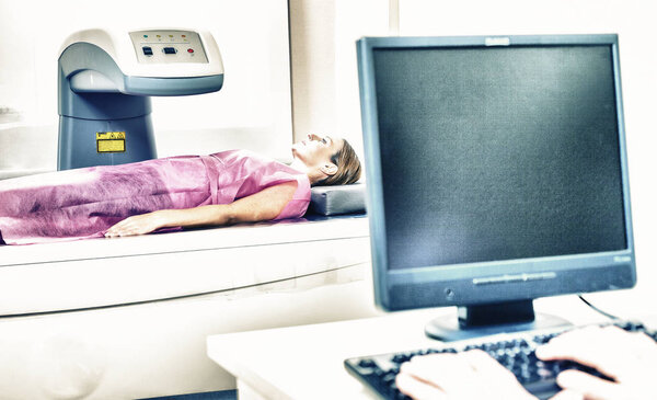 Woman in 40s undergoing medical x-ray with elderly doctor looking at monitor.