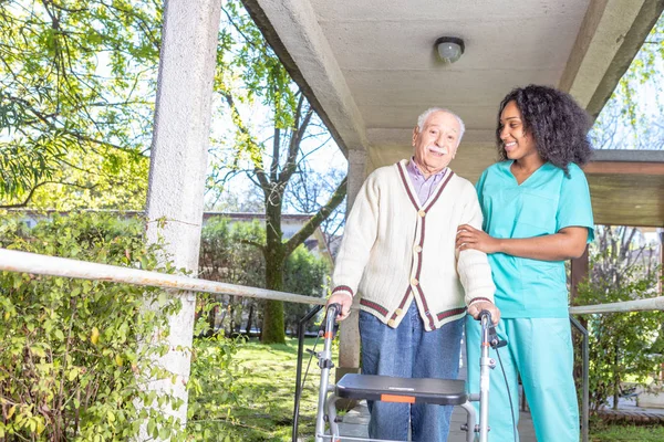 非洲护士帮助老人与沃克在康复设施走廊 — 图库照片