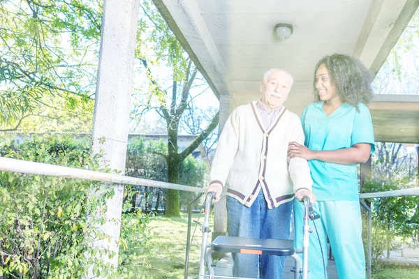 African Nurse Helping Elderly Man Walker Rehab Facility Hallway Light — Stock Photo, Image
