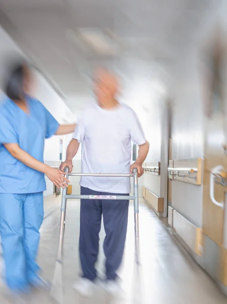 Asian doctor helping elder man with walker in hospital hallway.