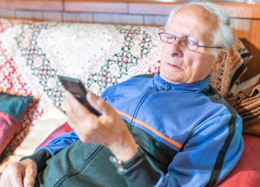 Cep telefonu evde seyir gözlüklü yaşlı adam.