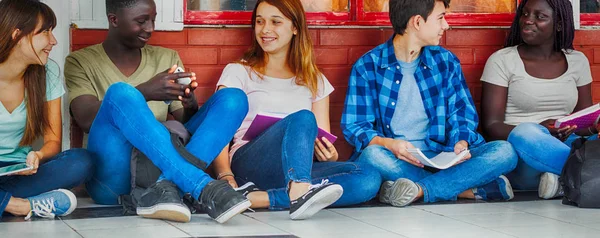 Group of multi ethnic teenagers seated in the hallway, talking each other.