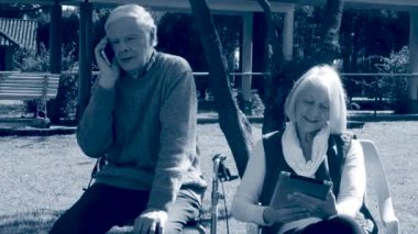 Yaşlı çift açık tablet kullanma ve cep telefonu için konuşurken oturmuş. Sepya tonlu