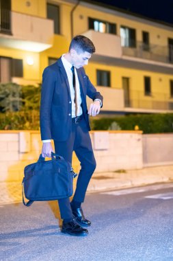 Genç erkek yönetici sabahın erken saatlerinde işe giderken çantasını taşıyor ve saatine bakıyor. İş konsepti.