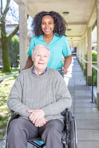 Elderly in the wheelchair is walking  accompanied by the nurse.