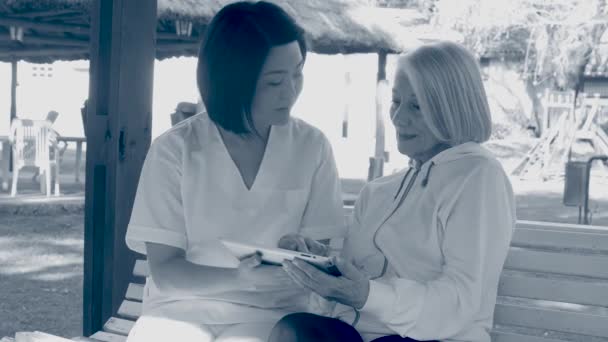 Медсестра Помогает Пожилой Женщине Пользоваться Планшетом Скамейке Сепия Тонизированная — стоковое видео