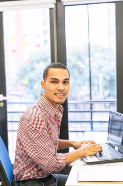 Genç çocuk ofiste dizüstü bilgisayar kullanıyor..