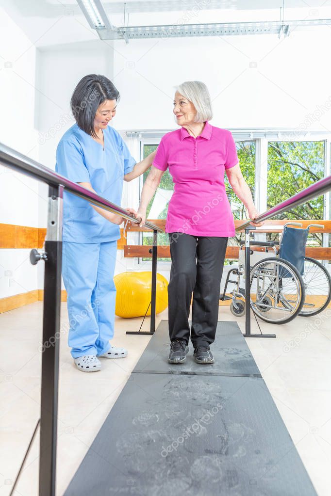 Elderly lady with walking problems training on the platform helped by the physiotherapist.