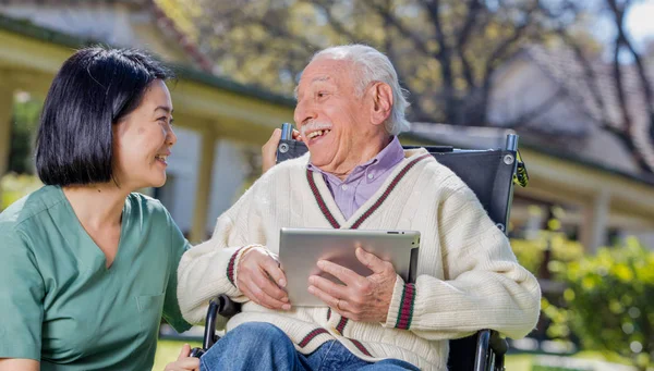 Nurse explaining use of tablet to elder people outdoor.