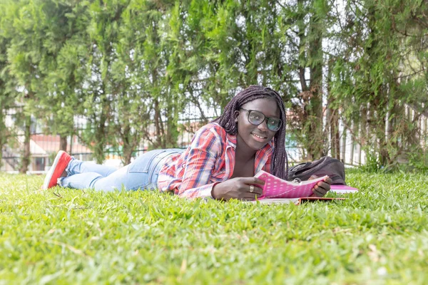 アフリカ系アメリカ人の少女が草の上に寝そべって学校の授業を — ストック写真