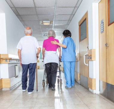 Rehabilitasyonda sopayla walker ve kıdemli adamla yaşlı bayan yardımcı fizyoterapist.