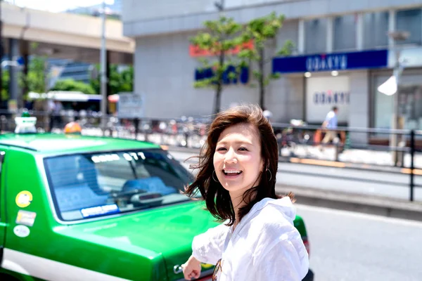 カメラを見て香港のダウンタウンでアジアの女性を笑顔と緑のタクシーを示す手を上げる — ストック写真