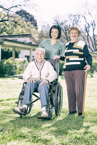 与护士一起在养老院花园中的老年夫妇 — 图库照片