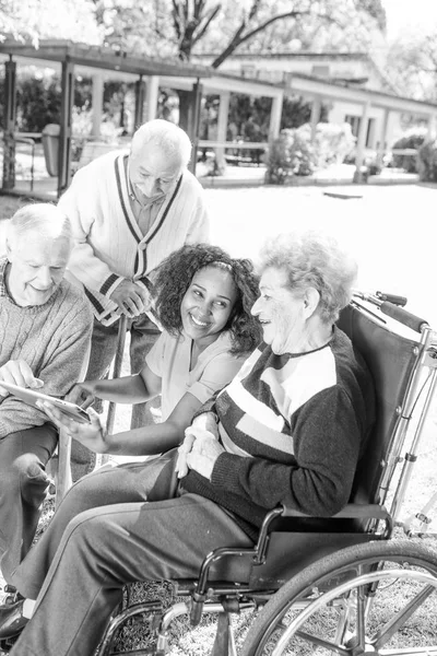 特別養護老人ホームの看護師の公園でリラックスした高齢者の笑顔のグループ — ストック写真