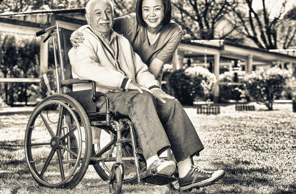 Asian and african nurses helping elder man on wheelchair at rehab facility garden.