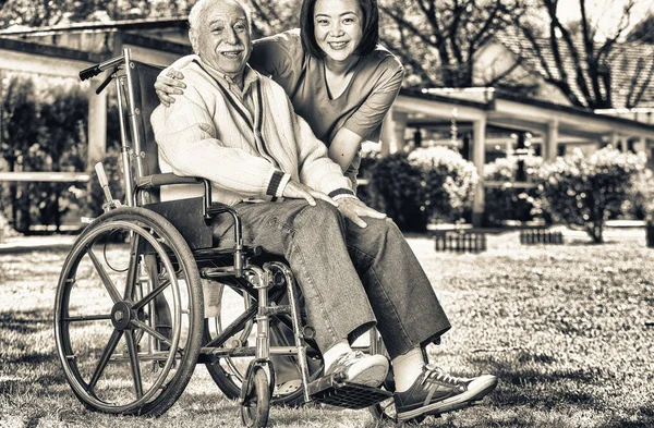 在康复设施花园帮助老人坐轮椅的亚洲和非洲护士 — 图库照片