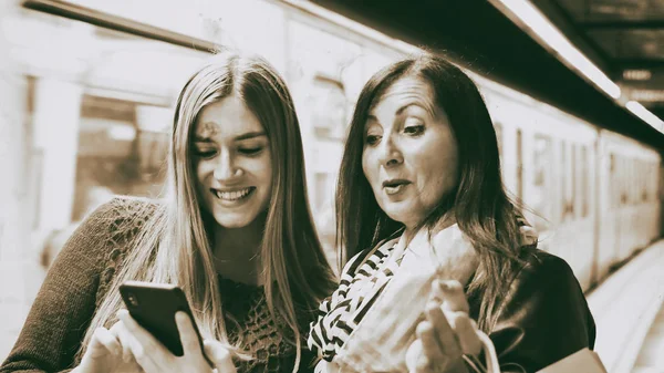 Couple of female friends looking to the phone in a subway statio — Stock Photo, Image