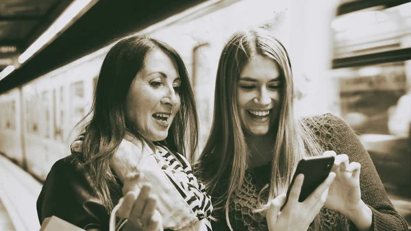Un par de amigas mirando al teléfono en una estación de metro — Foto de Stock