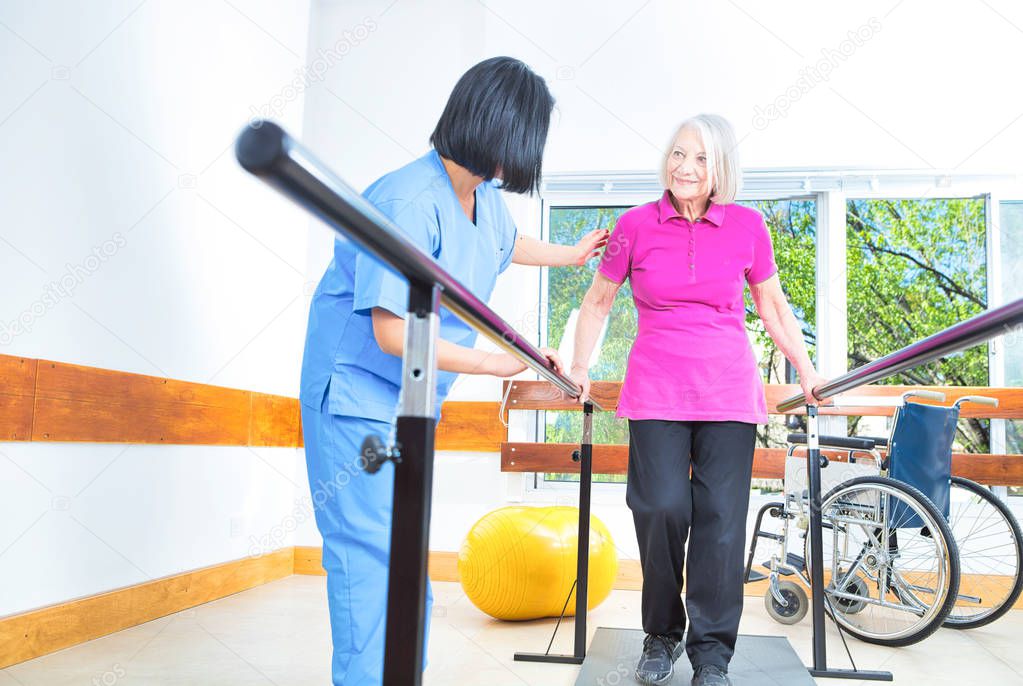 Asian nurse assisting aged senior woman training on the bars at 